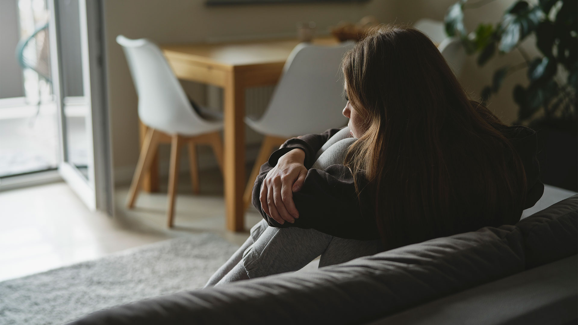 Mulher triste sentada no sofá abraçando as pernas representando o Impacto Psicológico das Sequelas de um acidente